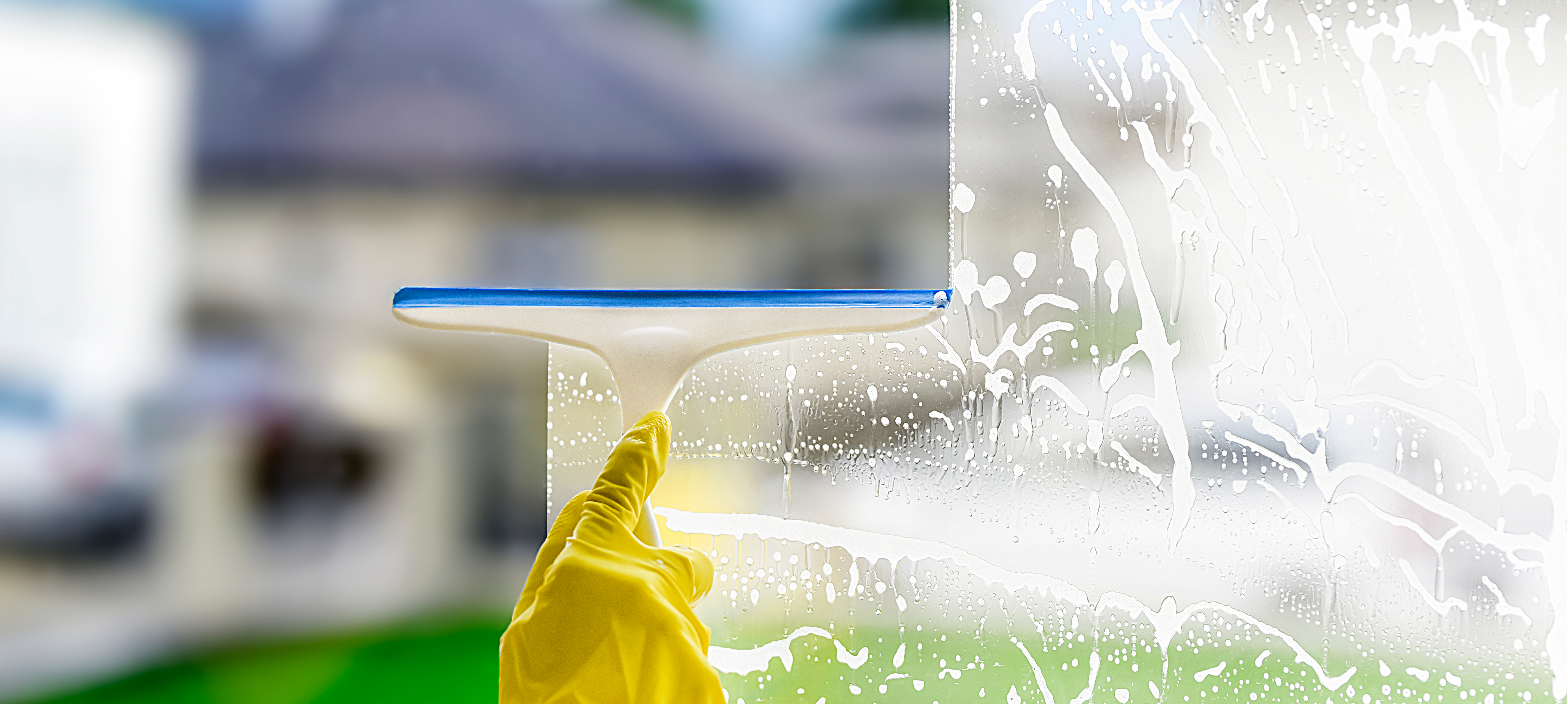a hand wearing a yellow glove cleaning windows with a wiper as part of the spring cleaning checklist