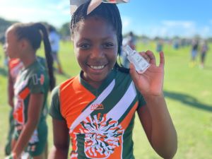 Young girl smiling while wearing a Miami Hurricanes outfit and holding a Cinch hand sanitizer