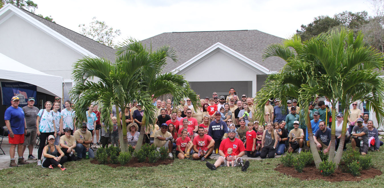 Sergeant Justin Callahan holding his youngest child posing with all the Homes For Our Troops volunteers in front of the house built for his family