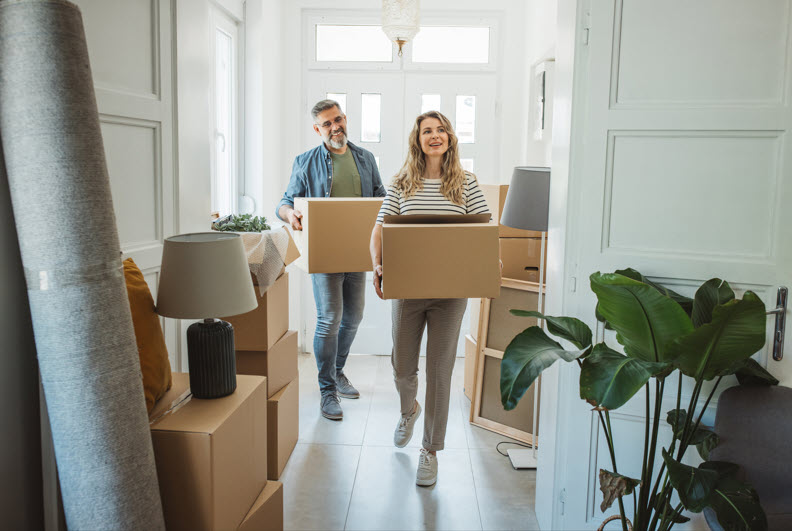 Mature couple smiling amidst moving boxes in their new home, symbolizing a fresh start with the security of a home warranty.