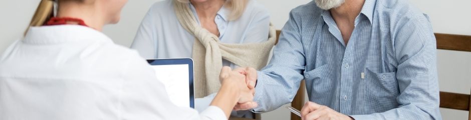 A real estate agent shaking a man's hand, whbo is sitting next to a woman 