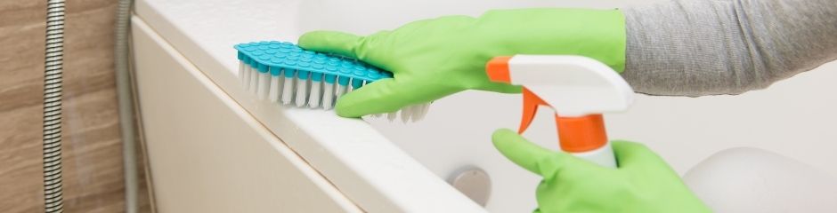 A woman in green gloves scrubbing her tub