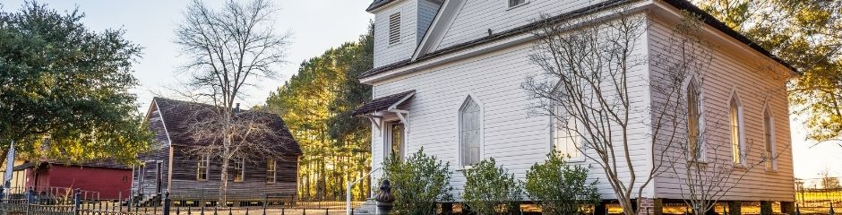 Three countryside houses amid tall trees in a warm sunset