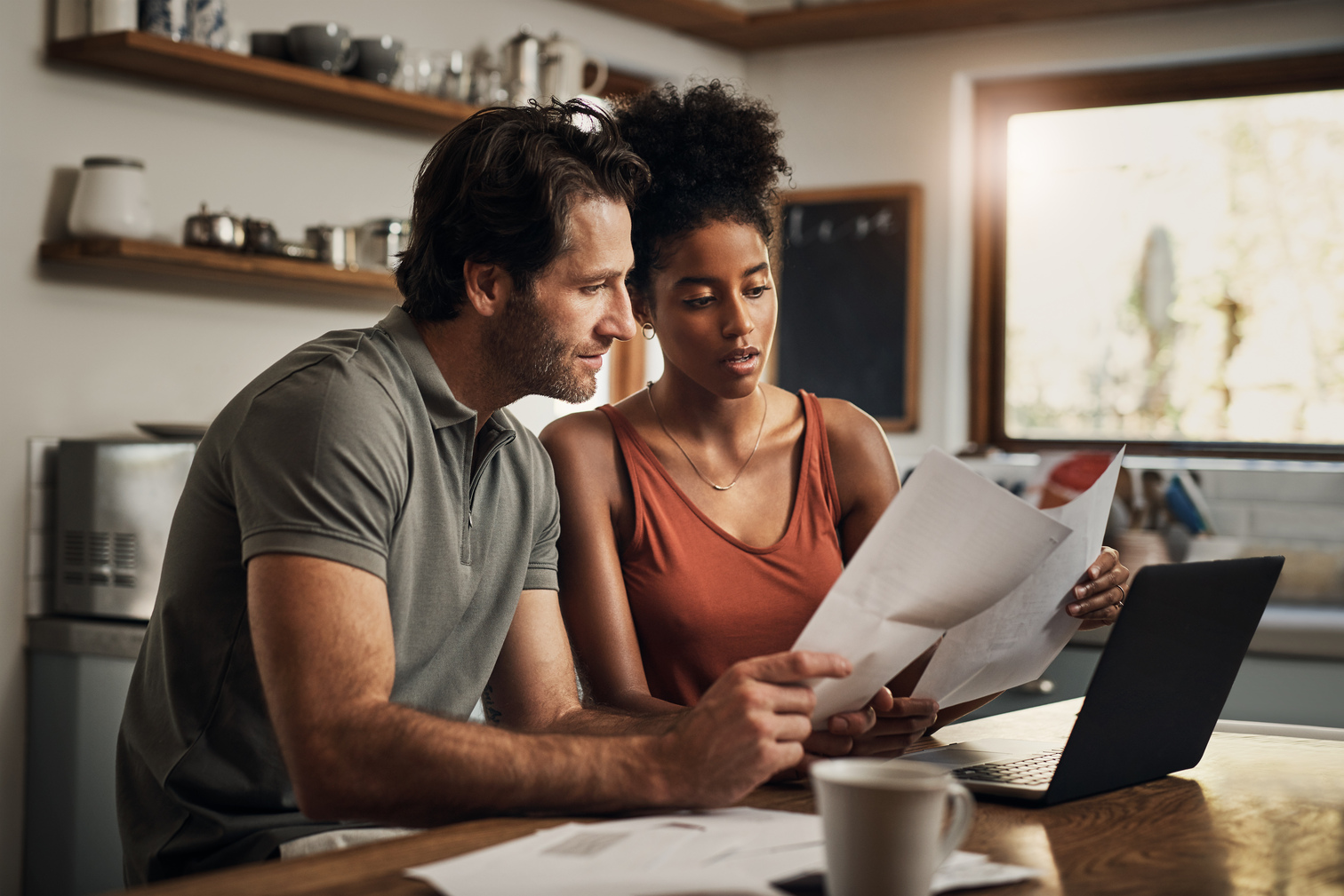 Interracial couple sitting at kitchen table looking over home warranty documents