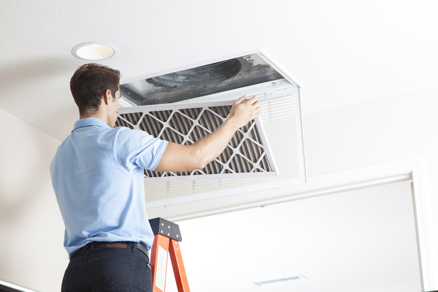 Repairman standing on a ladder replacing a ceiling air conditioner filter