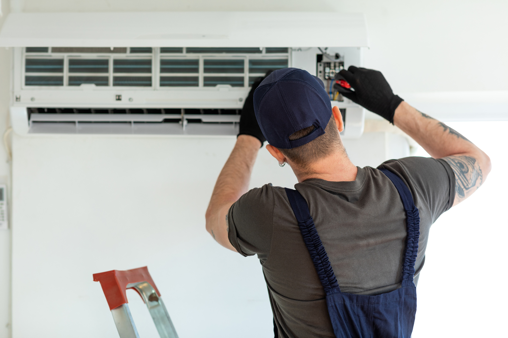 Repairman standing on a ladder fixing an air conditioner wall unit