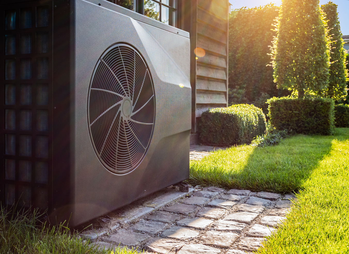 Outside air conditioner unit next to house sitting within the landscape and on a section of pavers