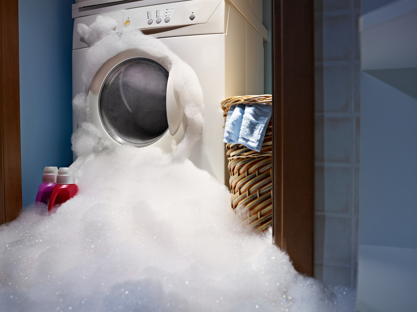 A malfunctioning front-loading washing machine with a large amount of suds pouring from the door