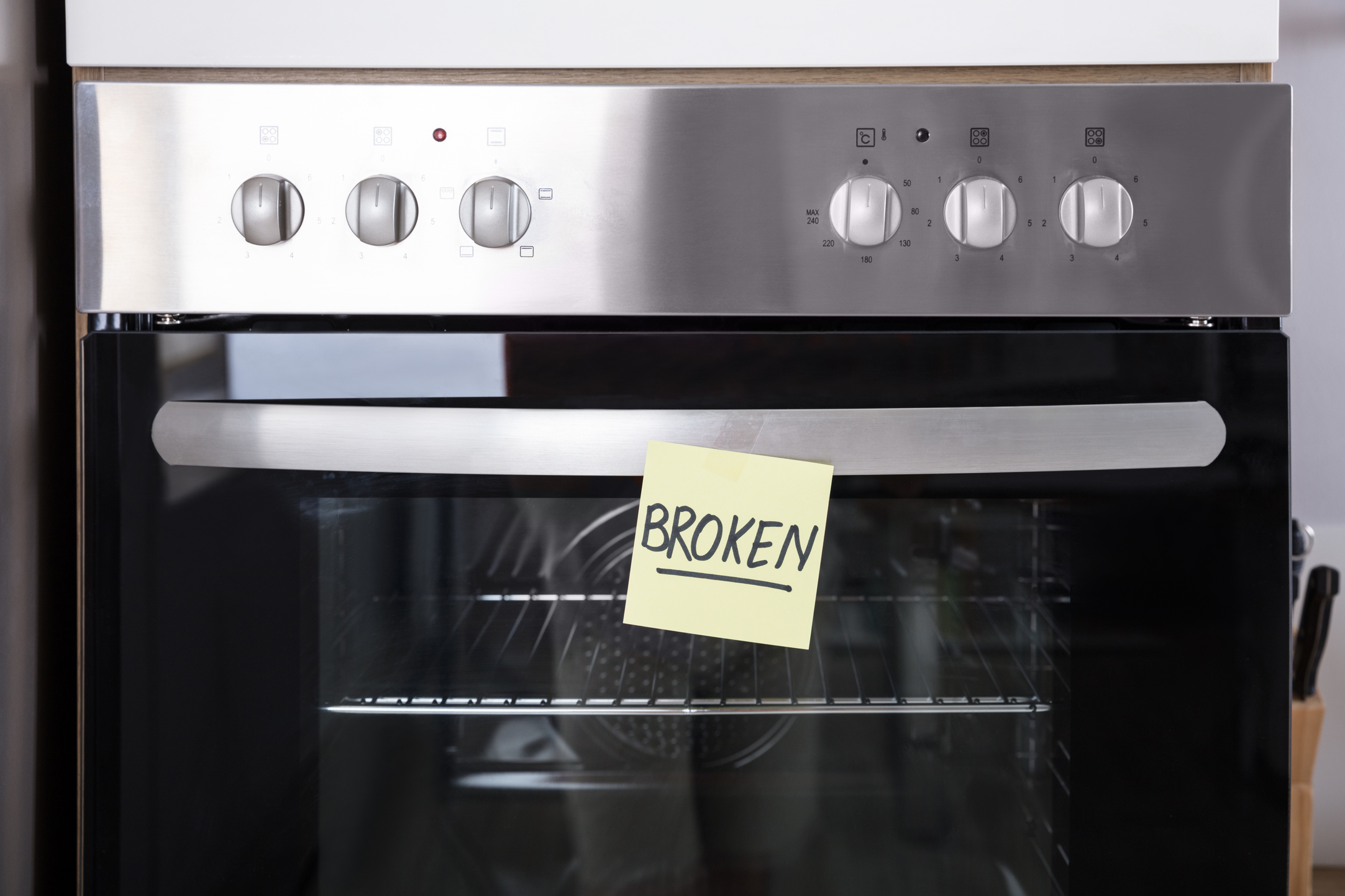 Close-up of a wall oven with a sticky note on the door with word broken in all caps and underlined