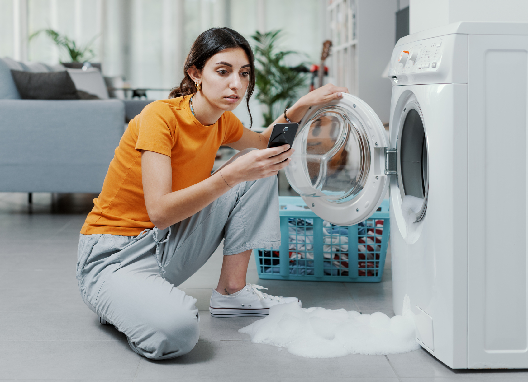 Woman looking at broken washing machine repair costs on her phone in her home