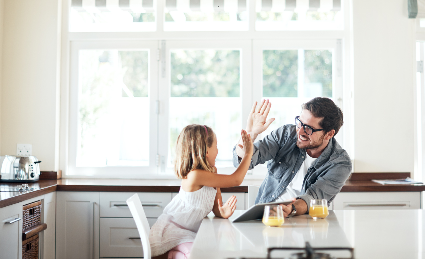 A father and daughter high fiving while sitting at the kitchen island