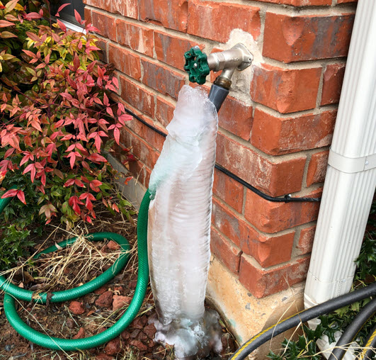 Block of ice covering a hose attached to a faucet on a brick house