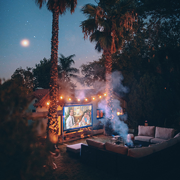 Outside movie screen surrounded by a couch, fire pit and trees