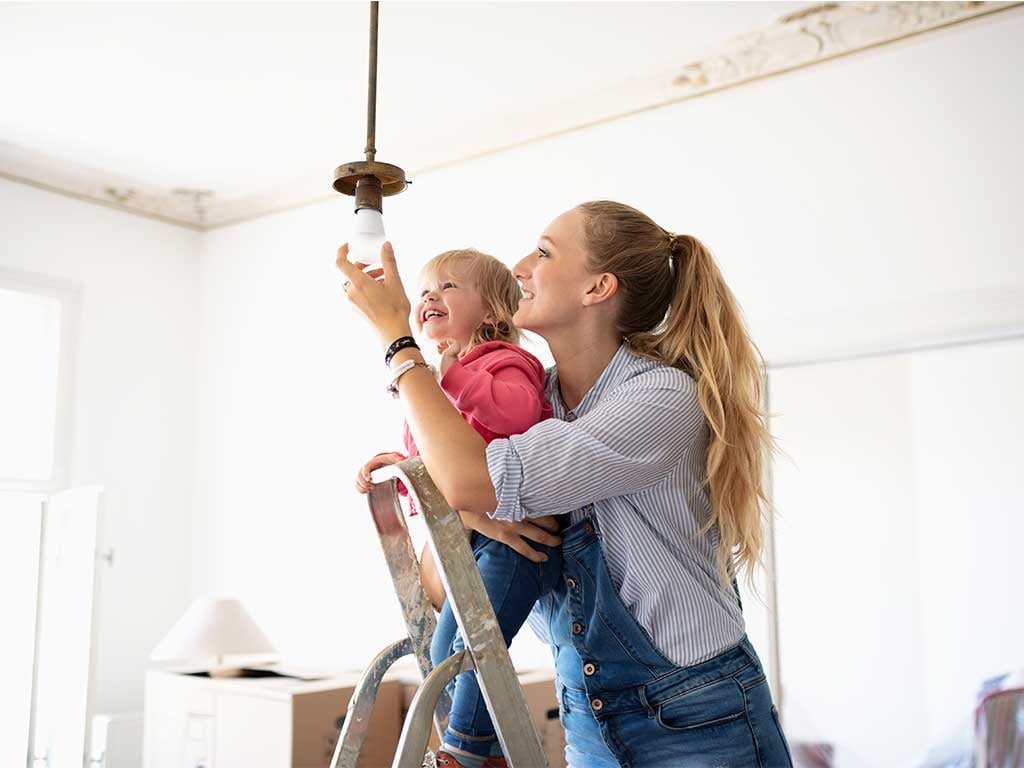 Smiling mom holding her toddler while installing light bulb