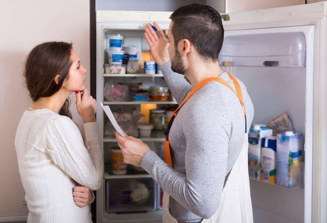 A service technician explaining the issues of a broken refrigerator to a woman