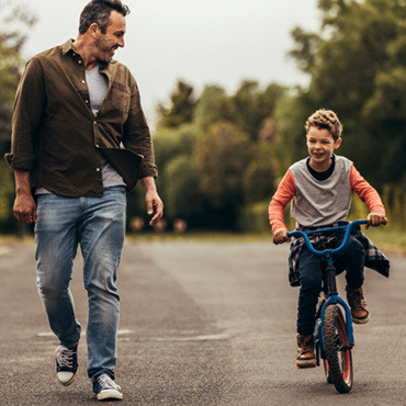 Father walking alongside his son riding a blue bike on the street