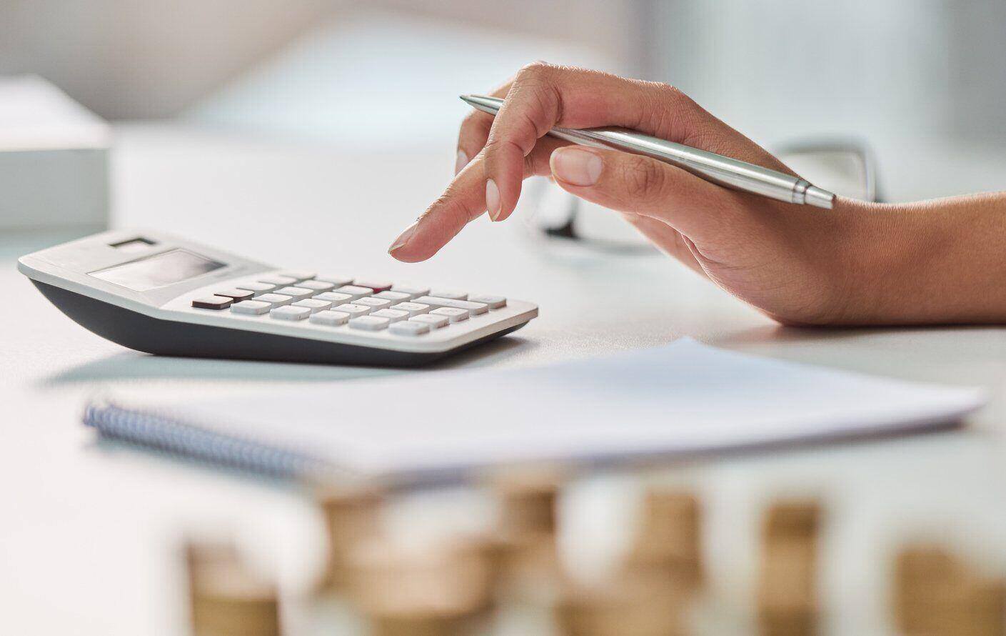 An image of a hand holding a pen and typing on a calculator