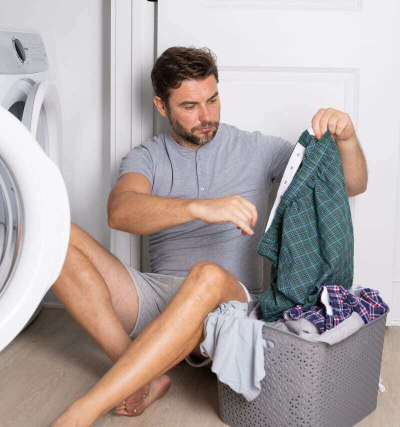 Man sitting on the floor pulling laundry out of basket to fill the open washing machine